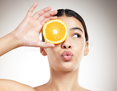 Buy stock photo Young happy mixed race woman pouting while holding an orange and posing against a grey studio background alone. Carefree hispanic female smiling showing a fruit while standing against a background