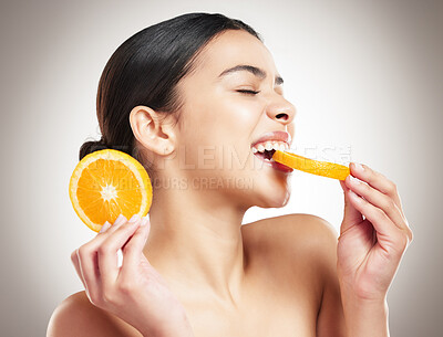 Buy stock photo Young happy beautiful mixed race woman eating an orange while posing against a grey background. One cheerful hispanic female eating a healthy fruit against a background