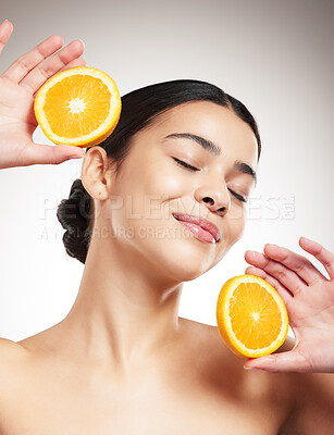 Buy stock photo Young happy beautiful mixed race woman holding an orange and posing against a grey studio background alone. Carefree hispanic female smiling showing a fruit while standing against a background