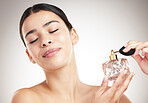 Young carefree mixed race woman spraying perfume while posing against a grey studio background. Hispanic female taking care of her skin against a background
