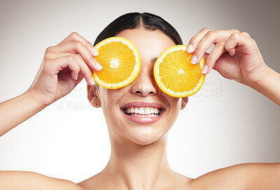 Buy stock photo Young happy beautiful woman covering her eyes while holding an orange and posing against a grey studio background alone. One hispanic female smiling showing a fruit while standing against a background
