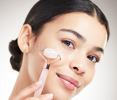 Buy stock photo Young happy mixed race woman holding and using a jade roller during her skincare routine while posing against a grey studio background. Carefree hispanic female taking care of her skin against a background
