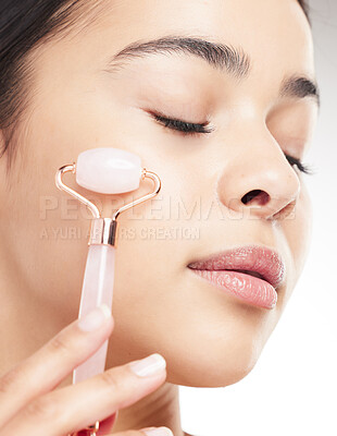 Buy stock photo Young carefree mixed race woman using a jade roller during her skincare routine while posing against a grey studio background. Hispanic female taking care of her skin against a background