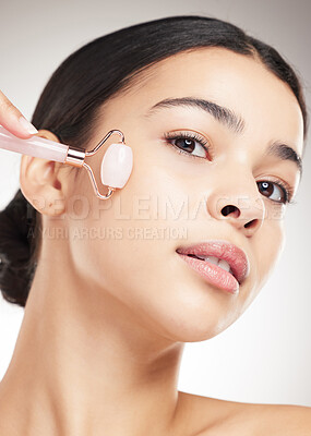 Buy stock photo Portrait of a young carefree mixed race woman using a jade roller during her skincare routine while posing against a grey studio background. Hispanic female taking care of her skin against a background