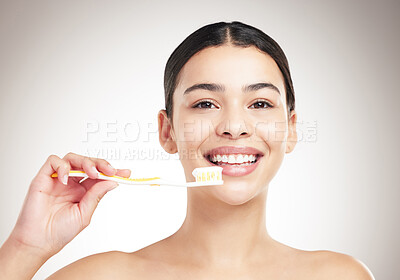 Buy stock photo Portrait of a young cheerful woman brushing her teeth standing against a grey studio background alone. One content female taking care of her dental hygiene while standing against a background