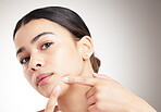 Beautiful young woman popping a pimple standing against a grey studio background alone. One female touching her face while standing against a background