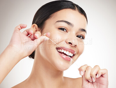 Buy stock photo Portrait of a young happy mixed race woman flossing her teeth while standing against a grey studio background alone. One hispanic female taking care of her dental hygiene while standing against a background