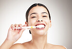 Portrait of a young cheerful woman brushing her teeth standing against a grey studio background alone. One happy female taking care of her dental hygiene while standing against a background