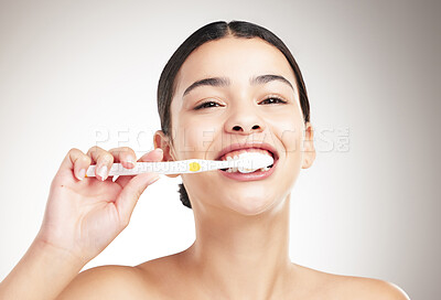 Buy stock photo Portrait of a young cheerful woman brushing her teeth standing against a grey studio background alone. One happy female taking care of her dental hygiene while standing against a background