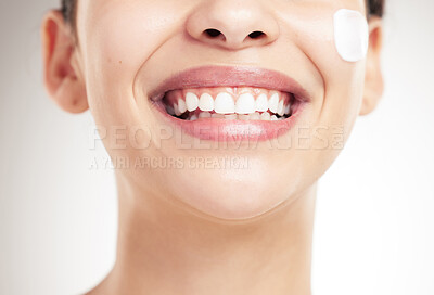 Buy stock photo Face of a beautiful woman showing her smile and teeth applying cream on her face posing against a grey studio background. Skincare is important. Taking care of dental hygiene