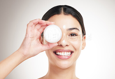 Buy stock photo Portrait of a young happy mixed race woman holding a lotion jar while standing against a grey studio background alone. One cheerful hispanic female applying cream to her body while standing against a background