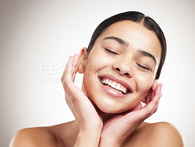 Young cheerful mixed race woman touching and feeling her face and posing against a grey studio background. Joyful hispanic female posing against a background