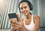 One fit young hispanic woman listening to music with headphones from a cellphone while taking a break from exercise outdoors. Happy athlete texting and using fitness apps online while browsing social media and watching workout tutorials