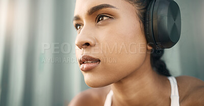Closeup of one fit young hispanic woman listening to music with headphones while exercising in an urban setting outdoors. Face of focused and motivated female athlete ready for training workout or run