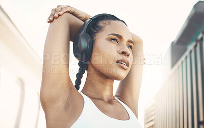 One fit young hispanic woman stretching arms for warmup to prevent injury while exercising in an urban setting outdoors. Focused and motivated female athlete listening to music with headphones while preparing body and mind for training workout or run