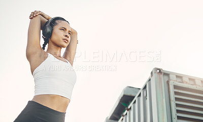 One fit young hispanic woman stretching arms for warmup to prevent injury while exercising in an urban setting outdoors. Focused and motivated female athlete listening to music with headphones while preparing body and mind for training workout or run