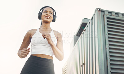 One active young hispanic woman from below listening to music with headphones while running in an urban setting outdoors. Happy female athlete doing cardio workout while exercising for better health and fitness