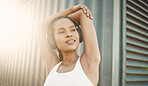 One fit young hispanic woman stretching arms for warmup to prevent injury while exercising in an urban setting outdoors. Happy and motivated female athlete listening to music with headphones while preparing body and mind for training workout or run