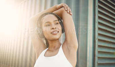 One fit young hispanic woman stretching arms for warmup to prevent injury while exercising in an urban setting outdoors. Happy and motivated female athlete listening to music with headphones while preparing body and mind for training workout or run