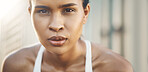 Closeup portrait of one fit young hispanic woman taking a rest break to catch her breath after a run or jog in an urban setting outdoors. Female athlete looking tired but determined after intense cardio exercise