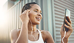 One fit young hispanic woman listening to music with earphones from a cellphone while taking a break from exercise outdoors. Happy athlete texting, making video call, browsing fitness apps and social media during workout in an urban setting