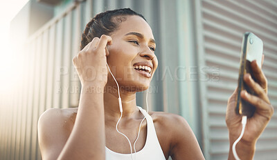 One fit young hispanic woman listening to music with earphones from a cellphone while taking a break from exercise outdoors. Happy athlete texting, making video call, browsing fitness apps and social media during workout in an urban setting