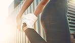 Closeup of one fit mixed race woman standing on one leg for warmup stretches to prevent injury while exercising in urban setting outdoors. Female athlete preparing quads and glutes for training workout or run