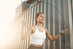 One fit young hispanic woman skipping with a rope while exercising in an urban setting outdoors. Happy athlete jumping while swinging a rope for cardio workout and warmup