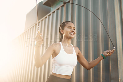 One fit young hispanic woman skipping with a rope while exercising in an urban setting outdoors. Happy athlete jumping while swinging a rope for cardio workout and warmup