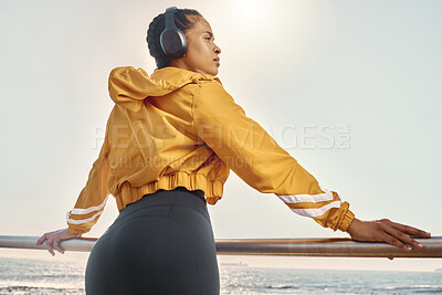 Fit young hispanic female athlete in sportswear listening to music with wireless headphones while taking a break from her early morning run along a promenade