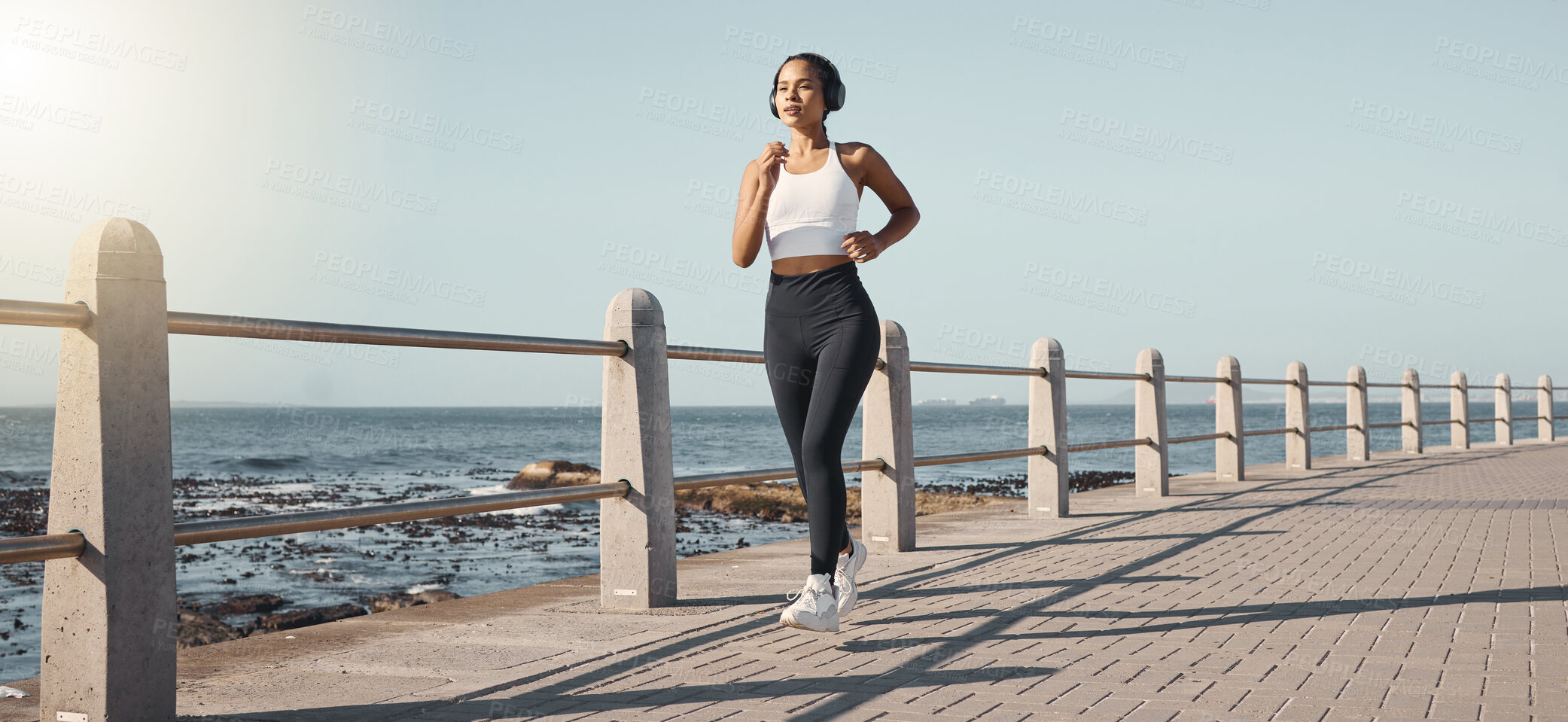 Buy stock photo Fitness, woman run at beach and with headphones listening to music for health wellness. Training or exercise, marathon or lens flare and female person running along the promenade listen to radio