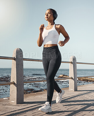 Buy stock photo Fitness, woman run at beach and with headphones listening to music for health wellness. Training or exercise, marathon or sportswear and female person running along the promenade listen to radio
