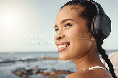 Close up of young mixed race female athlete looking happy and smiling while wearing headphones and listening to music while out for a run along the promenade. Exercise for a healthier mind and body