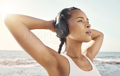 Close up of fit young female athlete listening to music on headphones while taking a break and stretching her arms behind her head