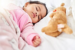 Adorable baby girl sleeping peacefully in bed with stuffed animal toy. Baby lying fast asleep on white bed with teddybear and wearing pink clothes and blanket. Mixed race newborn taking a routine nap 