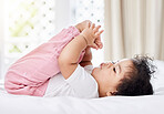 Cute little baby girl playing with her feet,lying on the bed in her bedroom. Small hispanic baby holding and looking at her feet and toes. Playful baby relaxing on her bed playing with her foot