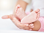 Closeup cropped view of a unrecognizable mixed race babies cute tiny soft feet and toes being held by the mother's hand. Woman holding the feet of her adorable newborn baby on a comfortable bed