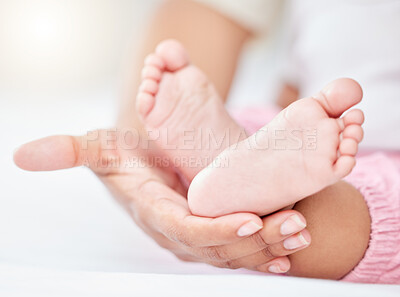 Closeup cropped view of a unrecognizable mixed race babies cute tiny soft feet and toes being held by the mother\'s hand. Woman holding the feet of her adorable newborn baby on a comfortable bed