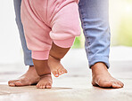 Low closeup of a mixed race parent and little baby daughters feet standing on the floor together at home. Mother teaching her little baby how to walk. Child learning to take their first steps