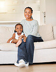 Happy and content young african american mother relaxing and bonding with her little daughter sitting on the couch in the lounge at home. Small girl smiling while enjoying time with her mom
