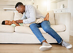 Young happy and cheerful african american father playing and bonding with his son on the couch in the lounge at home. Boy laughing and having fun with his dad on the weekend 