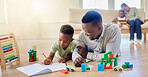 Young happy african american father helping his son with homework while sitting on the floor at home. Little boy focused on writing in a notebook and doing a task. Small boy drawing in a book
