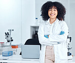 Portrait of a beautiful young african american woman with an afro wearing a labcoat and gloves while standing with her arms crossed in the laboratory. A mixed race female scientist smiling happily