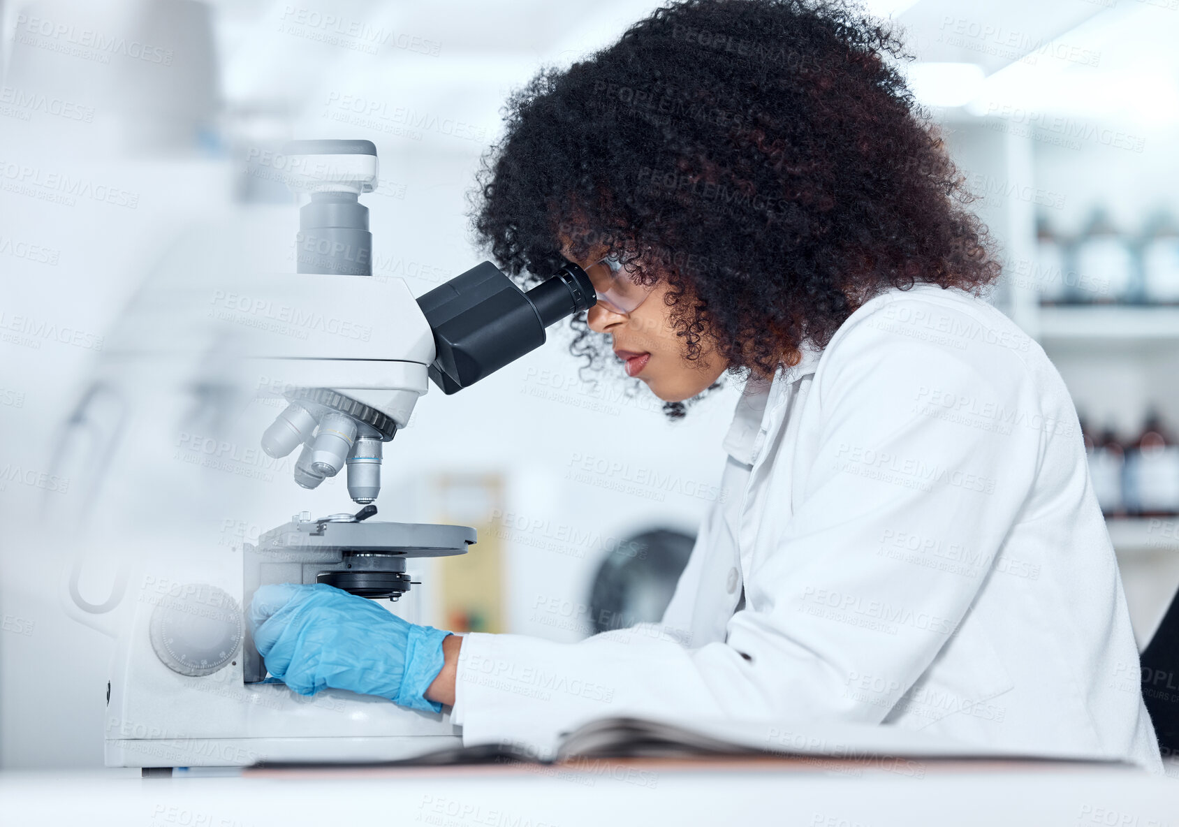 Buy stock photo One mixed race scientist with curly hair wearing safety goggles and gloves analysing medical test samples on a microscope in a lab. Young woman doing forensic research and experiment to develop a cure