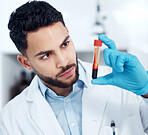 Closeup of a handsome mixed race young scientist holding a blood sample in a small glass tube container for research in a hospital. Young hispanic professional analyzing a sample in a laboratory while wearing protective gloves for hygiene purposes
