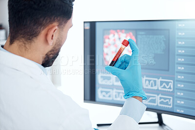 Unknown mixed race medical scientist sitting alone in a laboratory, holding a vial of blood and using a computer to examine it. Hispanic healthcare professional analysing a test tube sample in clinic