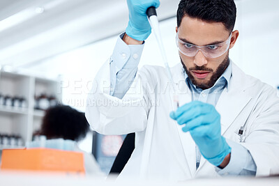 Buy stock photo One mixed race male scientist wearing safety goggles and a labcoat while conducting a medical research experiment with pipette and test tubes in a lab. Recording his findings for future investigation