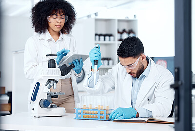 Two mixed race scientists wearing safety equipment while conducting medical research experiments with pipette and test tubes in a lab. Colleagues planning and recording data findings on digital tablet