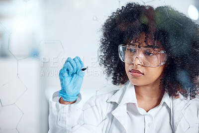 One serious young mixed race female scientist with a curly afro writing and planning on a glass board wearing glasses and gloves at work. Focused hispanic lab worker drawing on a board