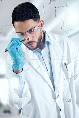 Buy stock photo One serious young mixed race male scientist writing and planning on a board wearing glasses and gloves at work. Focused hispanic lab worker drawing a formula on a board standing at work